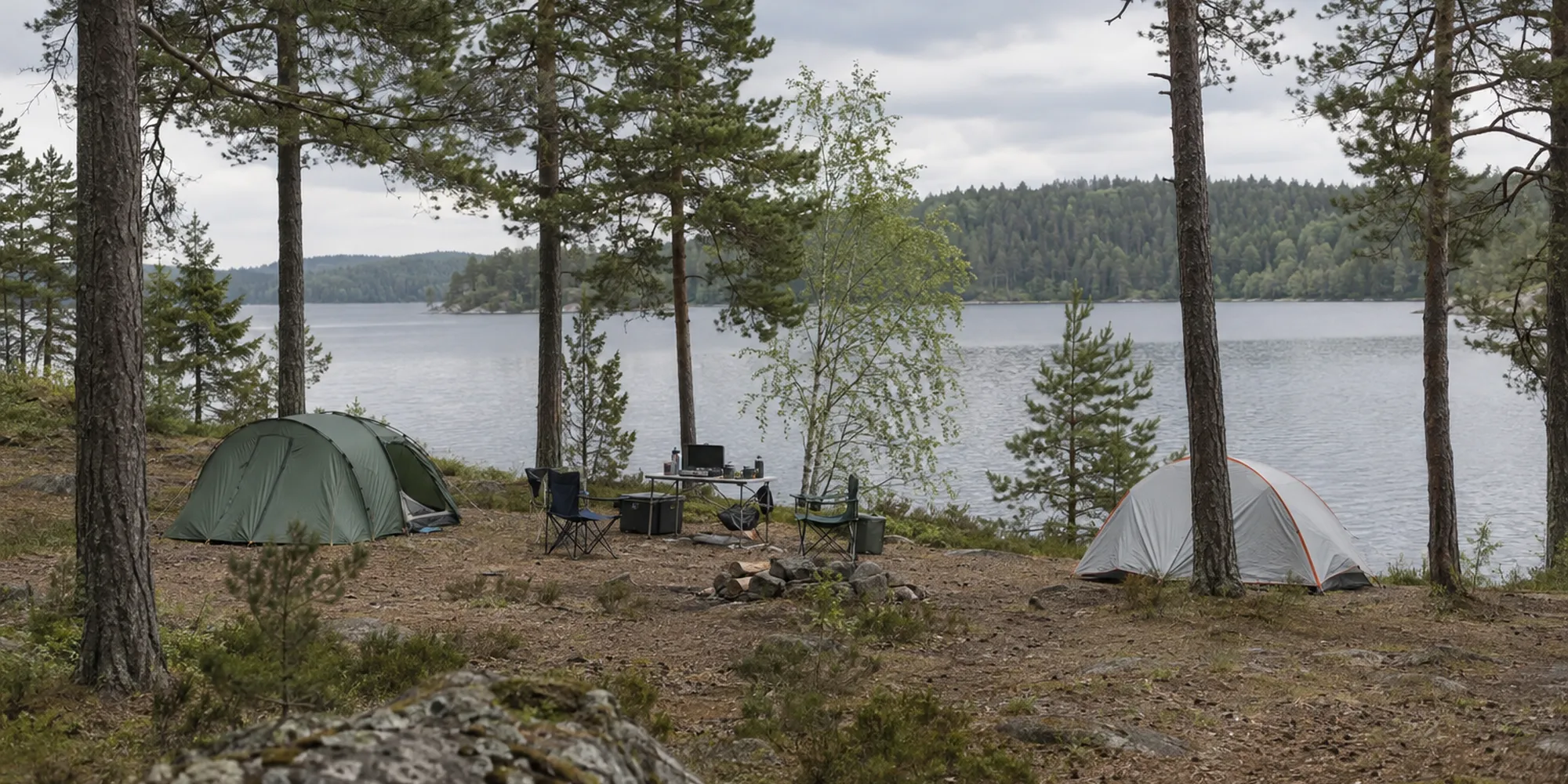 Lakeside forest campsite with tents, a camp table and folding chairs